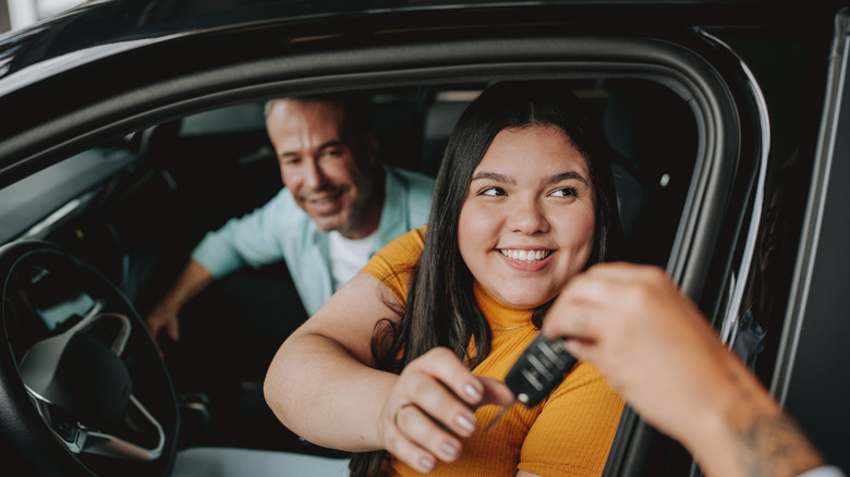 A couple seated in a car taking a set of car keys from a car salesman