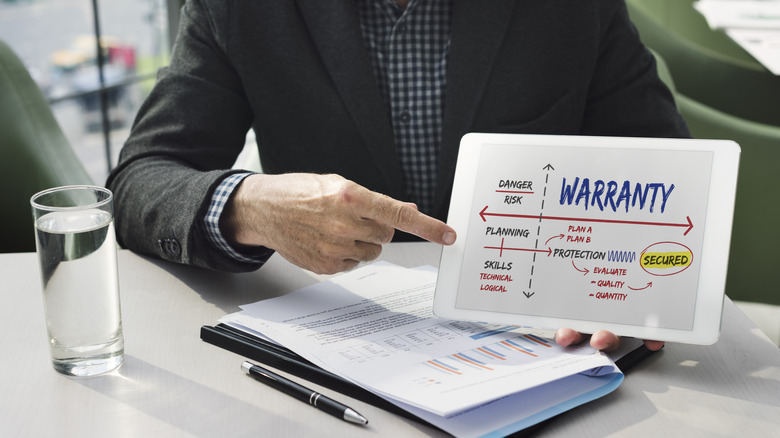 A man in a suit pointing at a tablet with a warranty on the screen