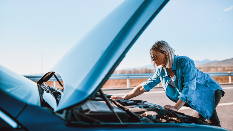 A woman looking under the hood of her car