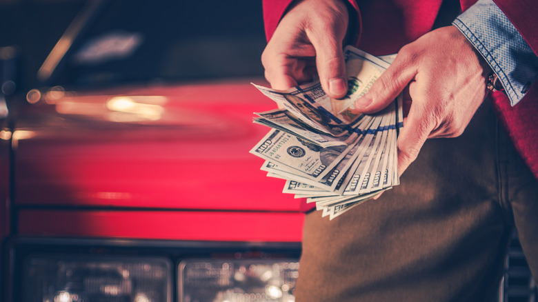 A pair of hands counting money in front of a car