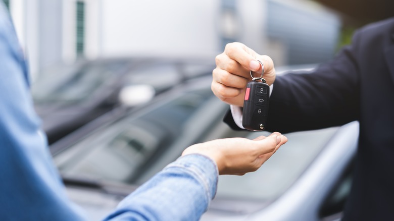A hand passing car keys to another person