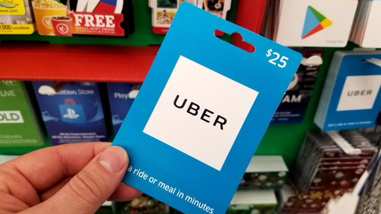 A hand holding an Uber gift card in front of a store display rack