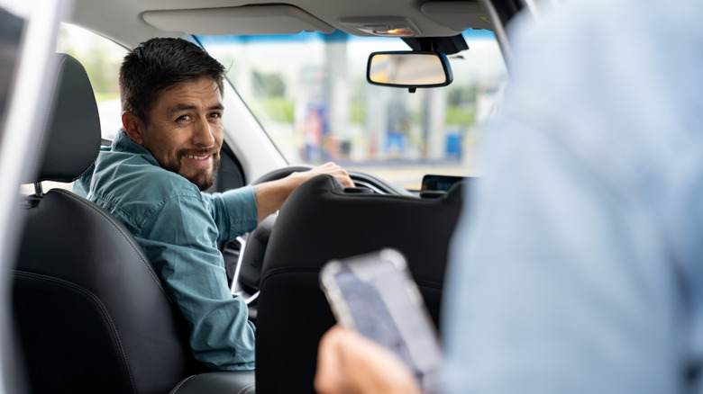 An Uber driver turning in his seat and smiling at a passenger