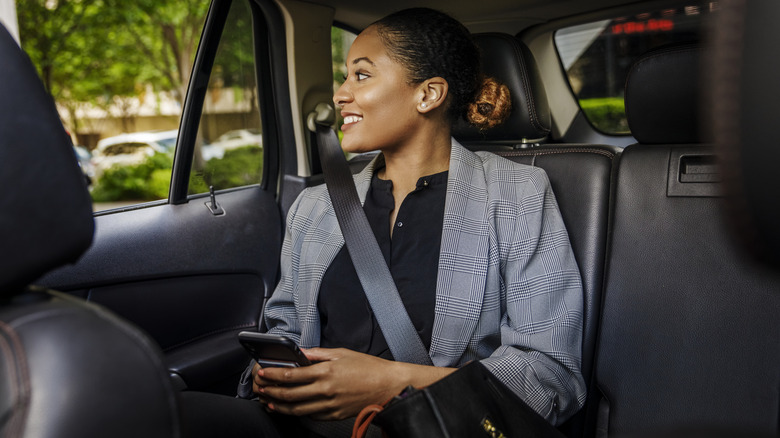 A smiling woman looking out a car's rear passenger window