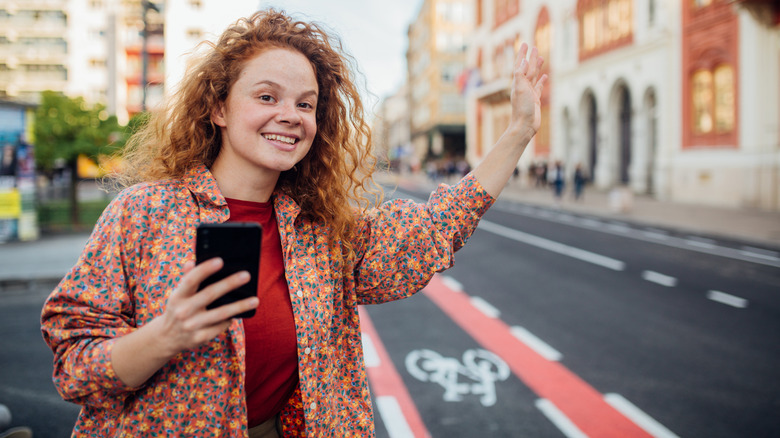 a woman holding a phone waving on a street corner