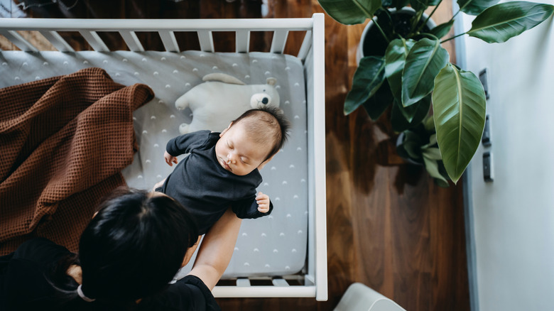 parent putting sleeping baby into crib