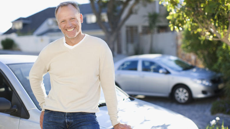 A man leaning against a car in a driveway