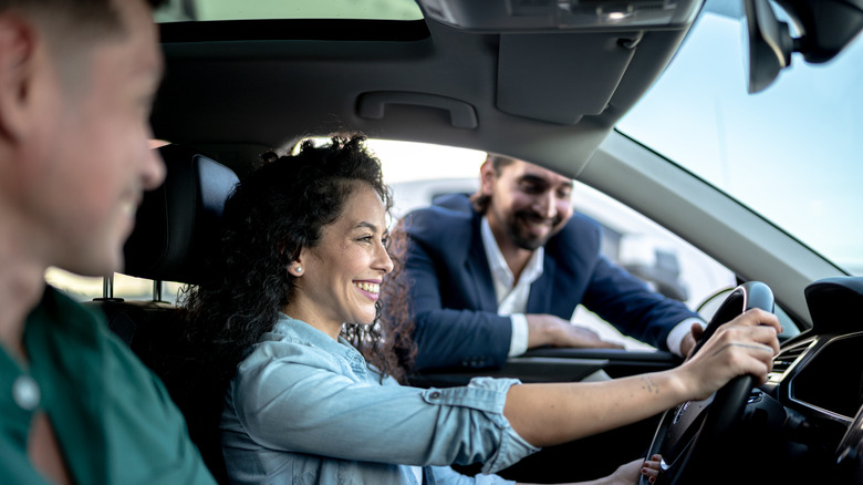 A smiling couple in a car with a salesperson