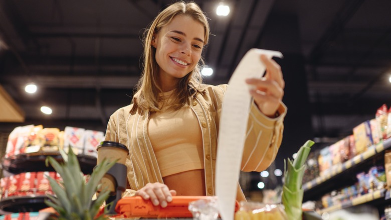 A woman grocery shopping holding a receipt