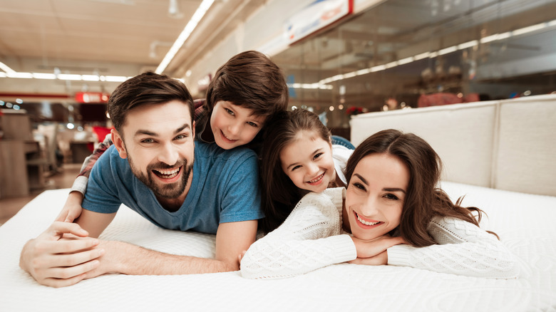 A smiling family laying on a bed in a furniture store