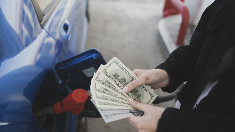 A pair of hands holding money in front of a gas pump