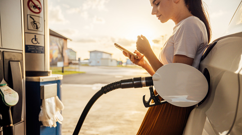 A woman texting while refueling her car