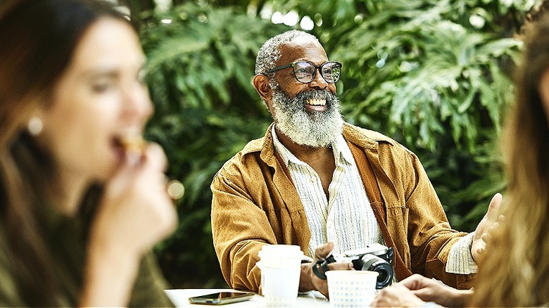 A smiling older man wearing glasses seated on an outdoor patio