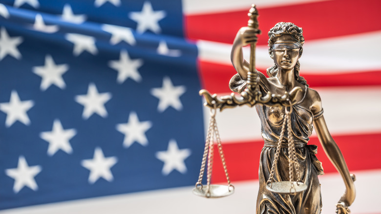 A statue of Lady Justice standing in front of the American flag.