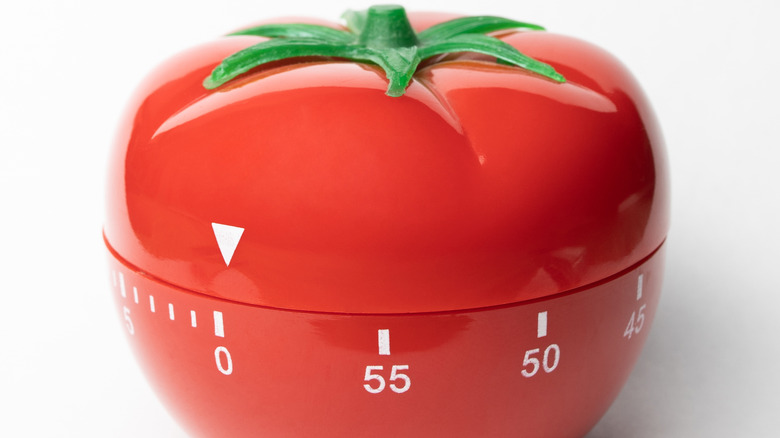 A close-up of the original, bright-red tomato kitchen timer that inspired the Pomodoro technique.