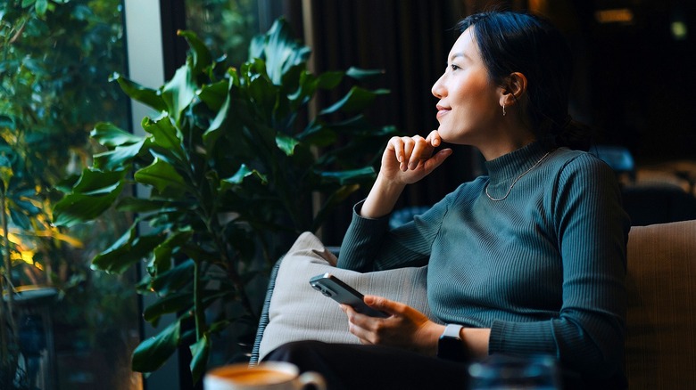 Woman wearing a green turtleneck and holding phone smiles while looking out window