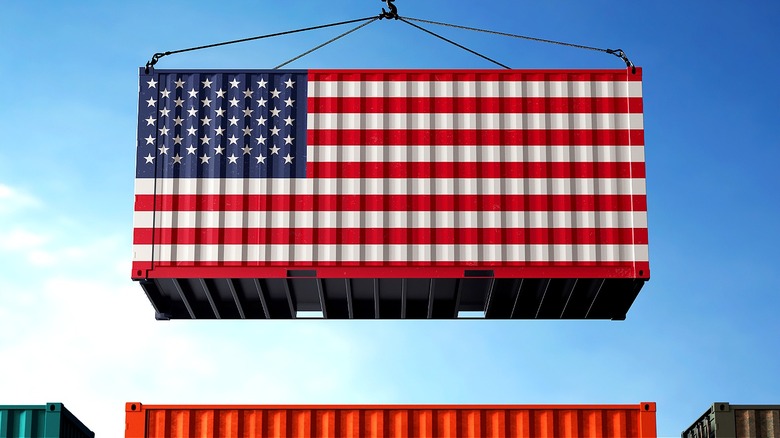 A U.S. flag shipping container hangs over other shipping containers