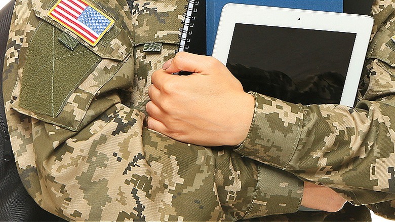 military person holding tablet, books