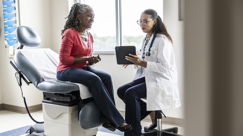 Female doctor and senior woman looking at digital tablet in exam room