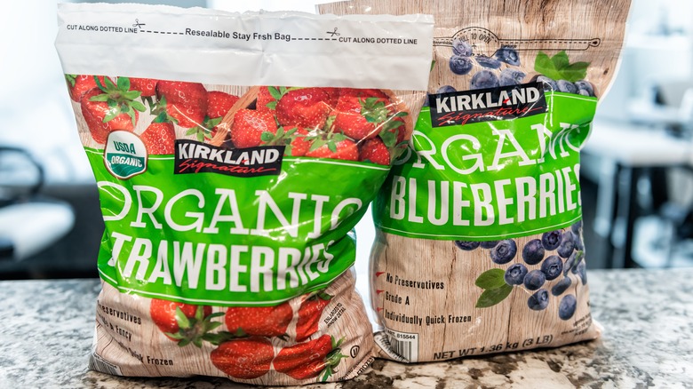 Two bags of Kirkland Signature frozen berries on a counter, under bright white light.