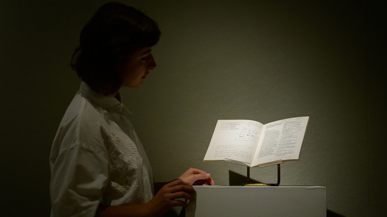 A woman looking at a book elevated on a pedestal under a spotlight