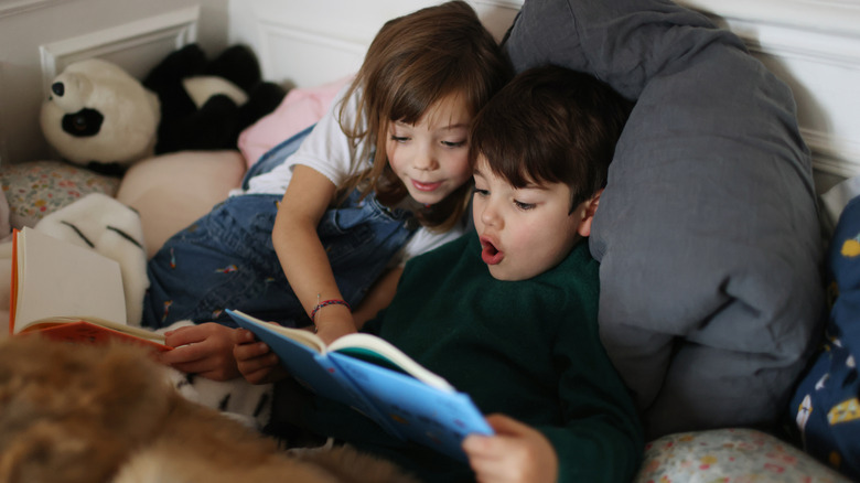 Two children laying in bed reading books with amazed expressions