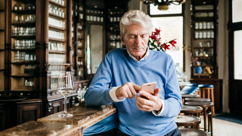 A distinguished elderly gentleman standing at a bar with his cellphone