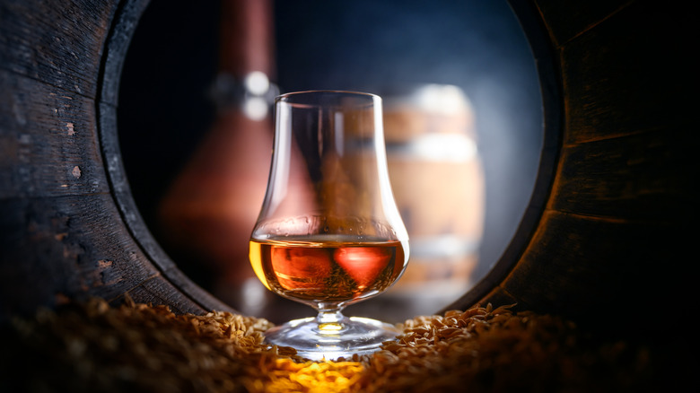 A glass of whiskey inside a dark empty whiskey barrel.