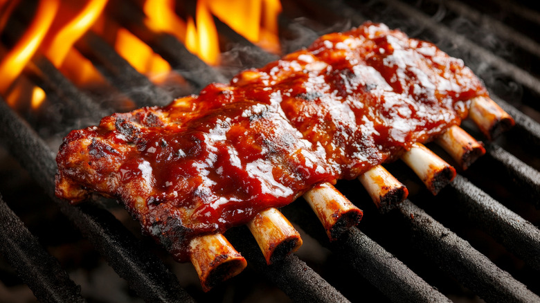 A rack of saucy ribs on a flame-grill barbecue, with oranges flames rising high.