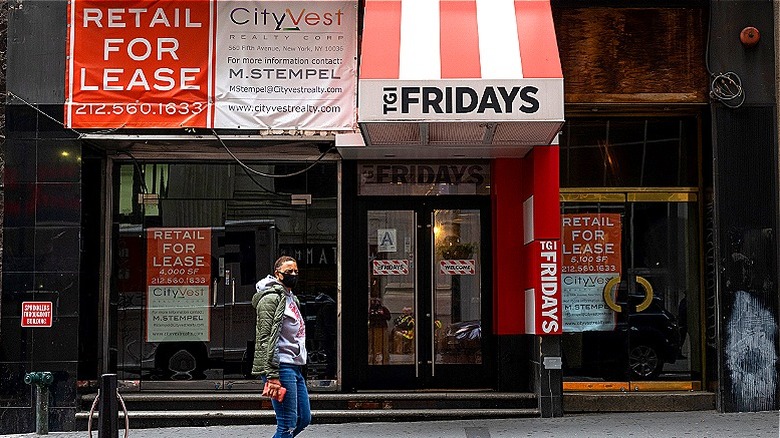 A woman wearing a mask walks by a closed TGI Fridays storefront