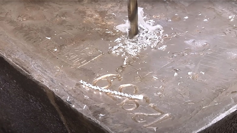 A power drill drills a hole through a bar of silver