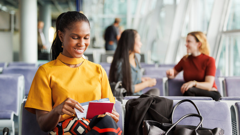 A woman looking at her passport and her flight ticket while in an airport lounge