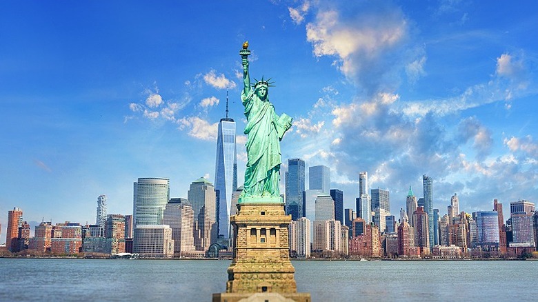 The Statue of Liberty with the New York City skyline in the background with a blue sky and scattered clouds above