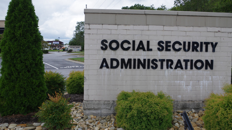 A decorative Social Security Administration wall, in landscaping, in front of a parking lot.