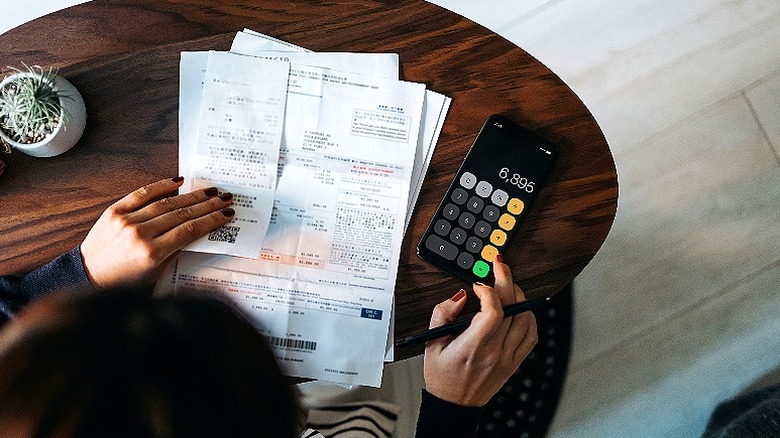 Person making calculations from pile of paperwork and calculator at wooden table