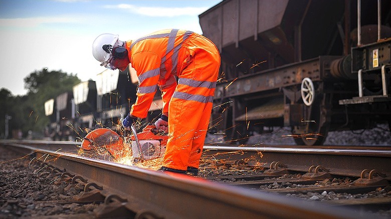 Sparks coming off of power tool as worker cuts into railroad track