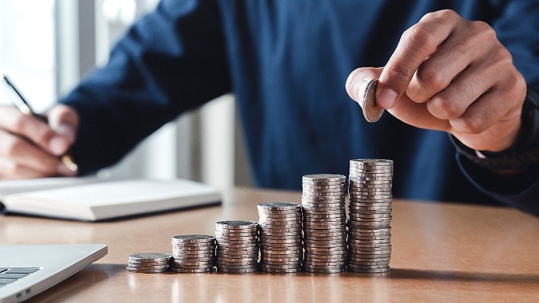 Person adds a coin to the highest stack in a group of six ascending coin stacks