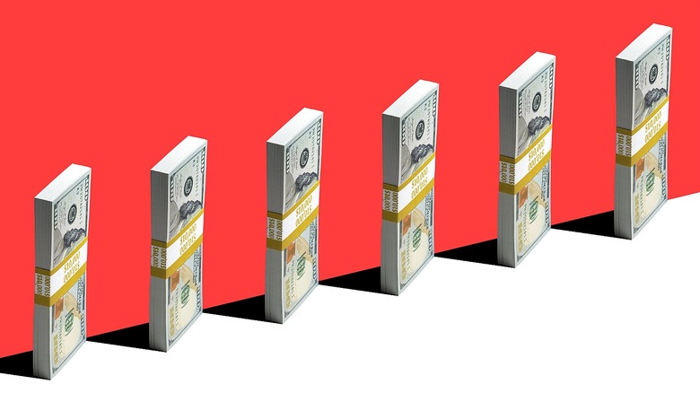 Six stacks of $100 bills standing on their end casting a shadow along a red wall