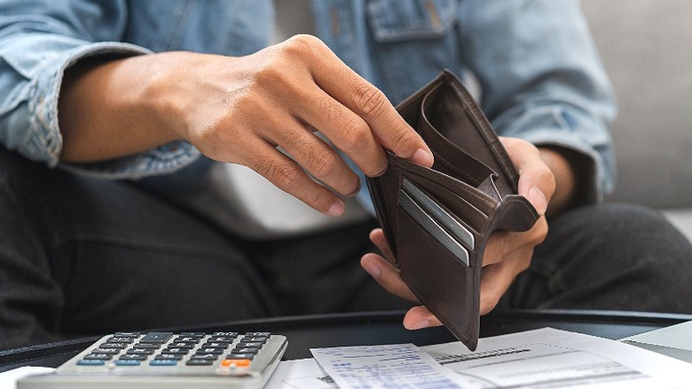 A man looks in empty wallet while at table with calculator and receipts