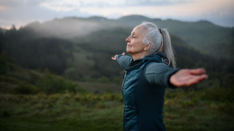 Senior woman doing breathing exercise in nature on early morning