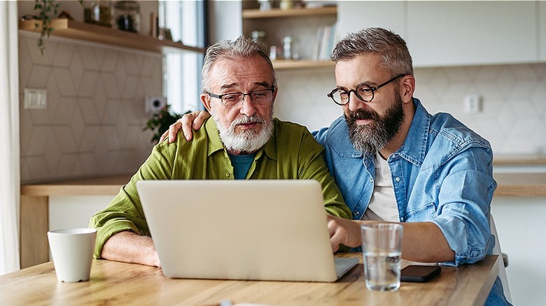 Two men sitting at kitchen table read from laptop