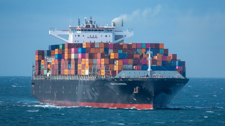 A shipping freighter stacked high with colorful shipping containers sails the open seas.