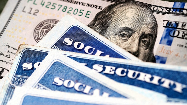 Four Social Security cards sitting atop a U.S. $100 bill