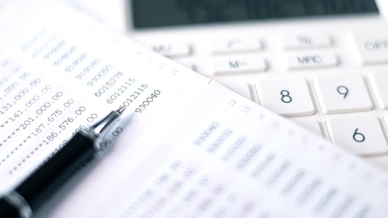 A sheet of white paper with a list of numbers printed on it laying over a white calculator