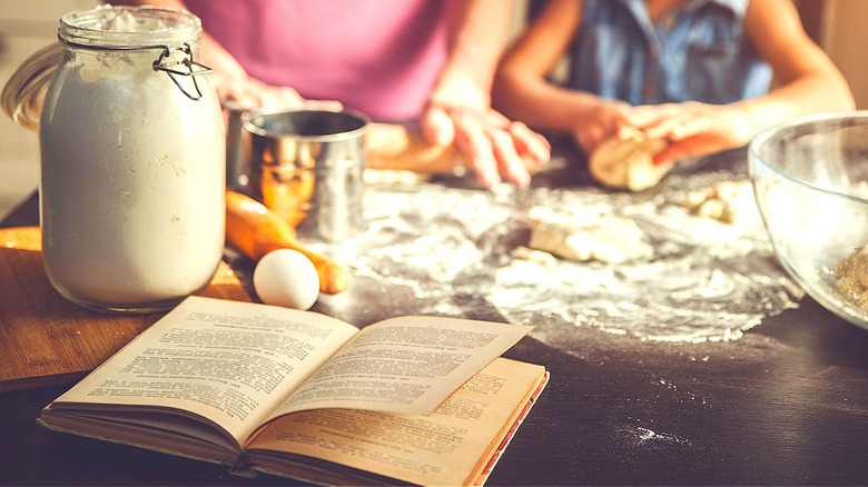 Cookbook in foreground, people cooking