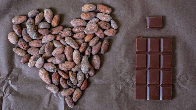 Cocoa beans in a heart shape next to a chocolate bar