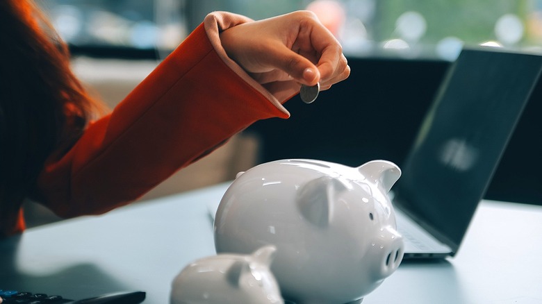 Hand holding coin about to add it to piggy bank