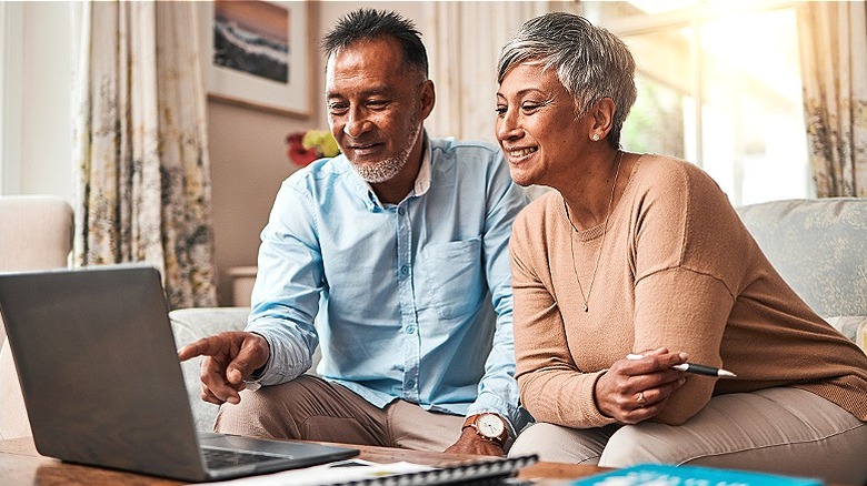 Couple smiling while looking at computer together in living room