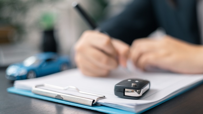 Person signing paperwork next to car key