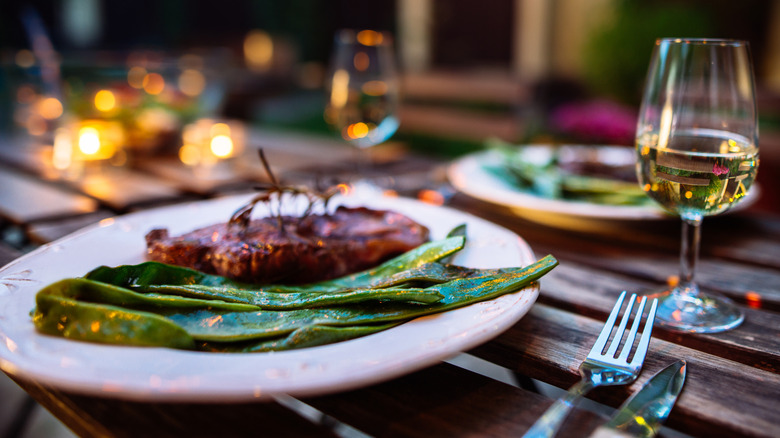 A romantic table setting for two, featuring a steak-and-greens dinner with wine.